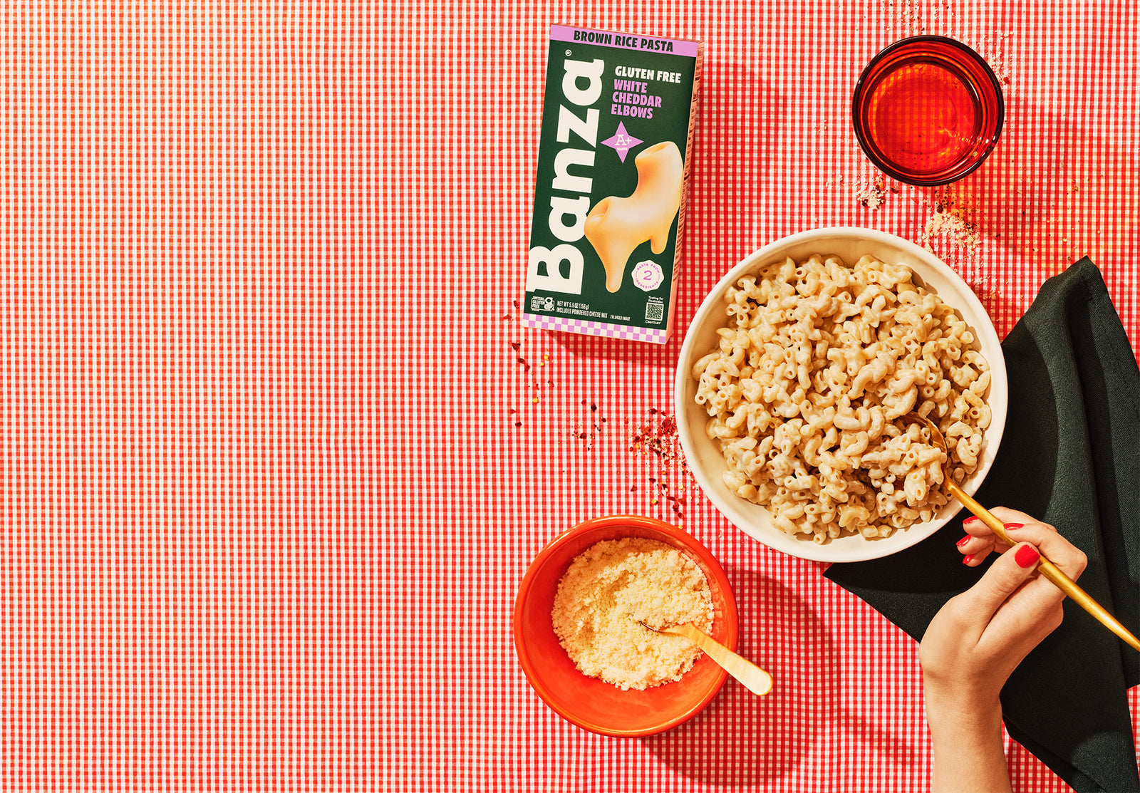 Bowl of cereal with a box of Banza gluten-free brown rice pasta on a red checkered tablecloth.